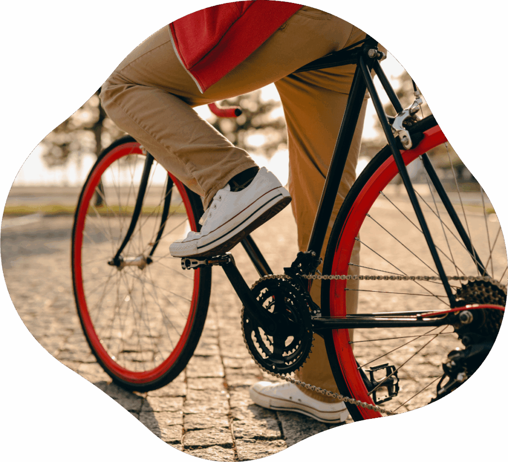 Junger Mann mit rotem Pullover und weißen Sommerschuhen auf City-Bike mit roten Fahrradfelgen im Park