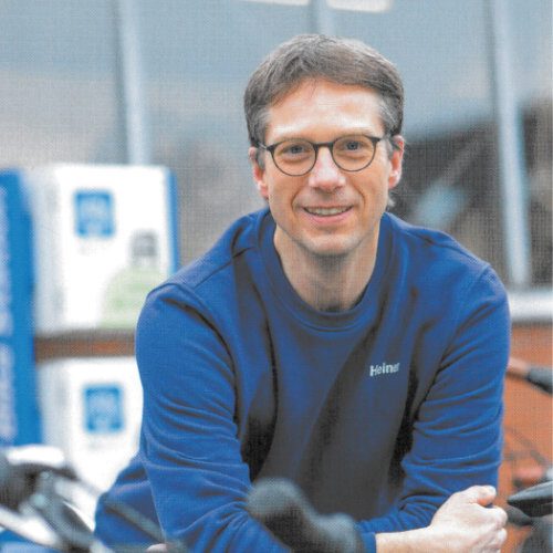 Firmeninhaber mit Brille und blauem Hemd über Fahrräder gebeugt lächelt